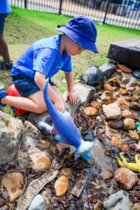 Pre-school Kindergarten child playing with dinosaur in rocky garden at Suncoast Little Learners